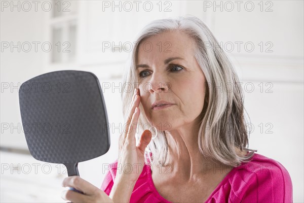 Caucasian woman looking at skin in mirror
