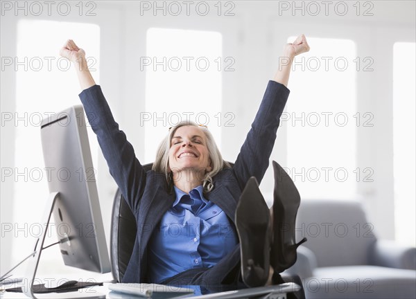 Happy Caucasian businesswoman with feet up on desk