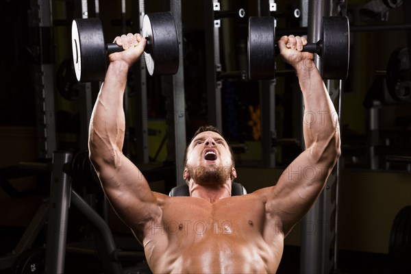 Caucasian man doing incline chest presses with dumbbells in gym