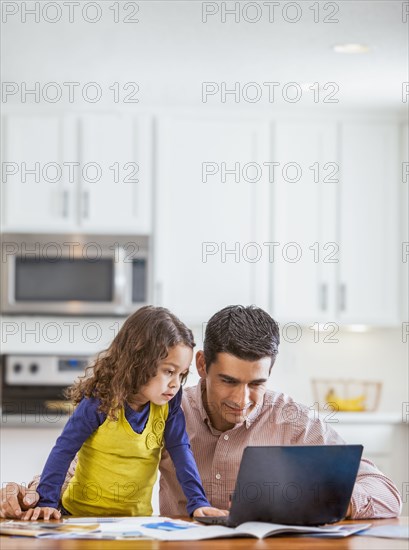 Father and daughter using laptop in kitchen