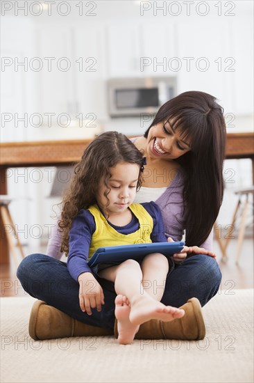 Mother and daughter using tablet computer on living room floor