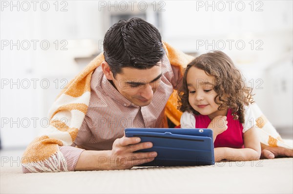 Father and daughter using tablet computer on living room floor