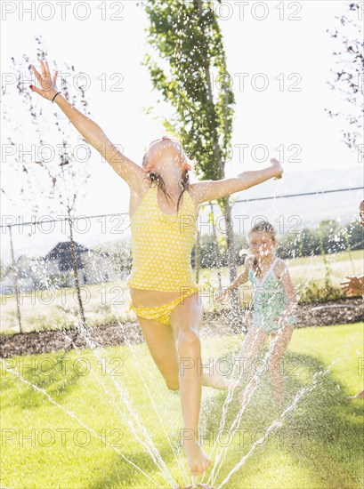 Caucasian girls playing in sprinkler in backyard