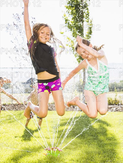 Caucasian girls playing in sprinkler in backyard