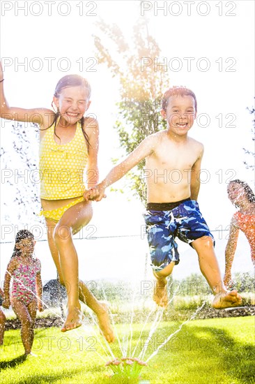 Caucasian children playing in sprinkler in backyard