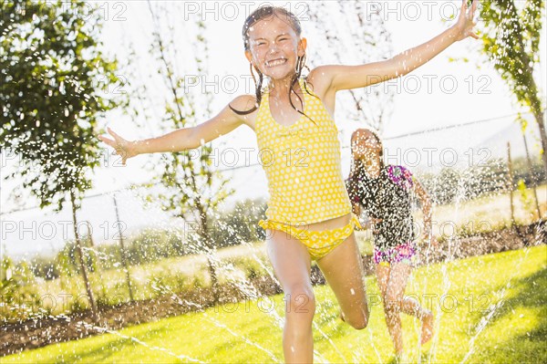 Caucasian girls playing in sprinkler in backyard