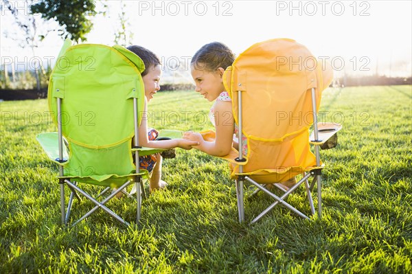 Caucasian children relaxing in lawn chairs in backyard
