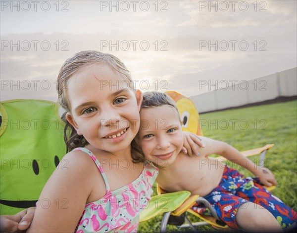 Caucasian children relaxing in lawn chairs in backyard