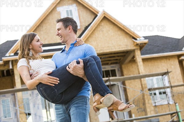 Caucasian man carrying woman near house under construction