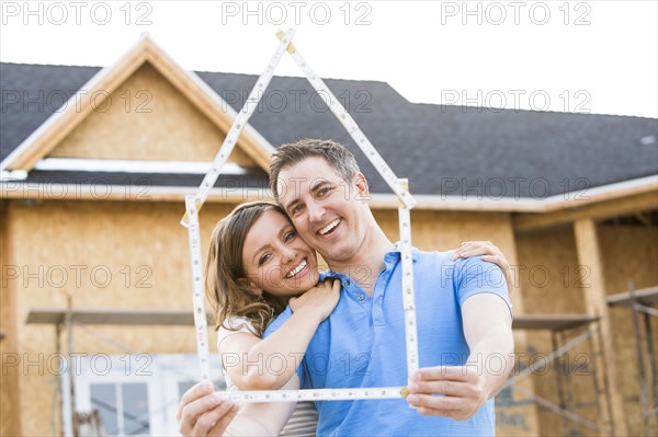 Caucasian couple holding frame near house under construction