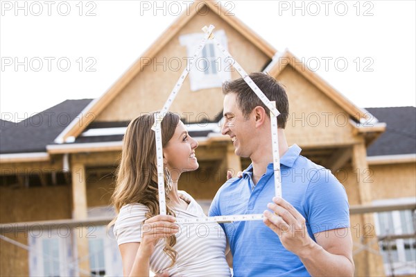 Caucasian couple holding frame near house under construction