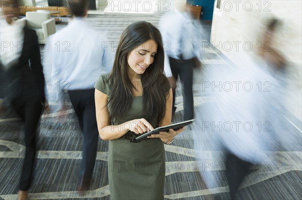 Businesswoman using digital tablet in busy office lobby