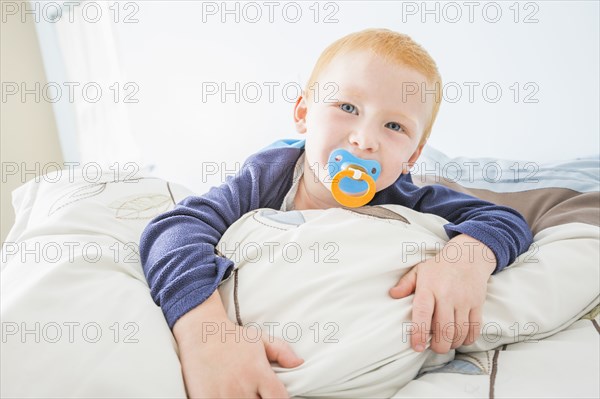 Caucasian boy sucking pacifier in bed