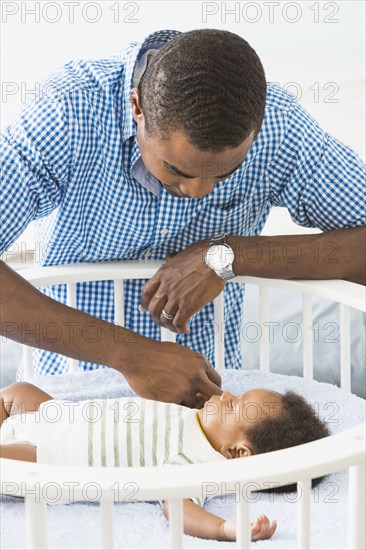 Father admiring sleeping baby son in crib