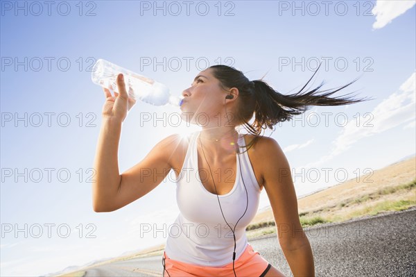 Caucasian runner drinking water bottle on remote road