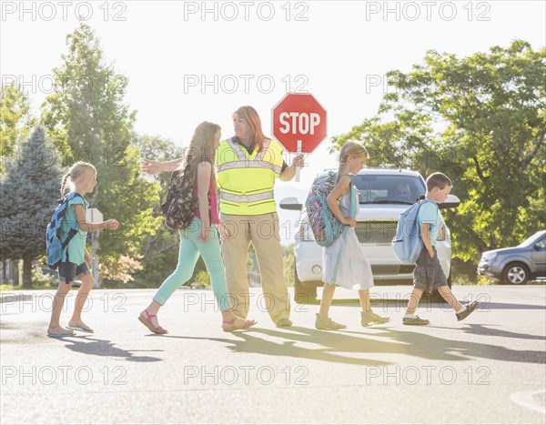 Caucasian crossing guard helping children in crosswalk