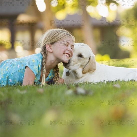 Caucasian girl nuzzling pet dog on grassy lawn
