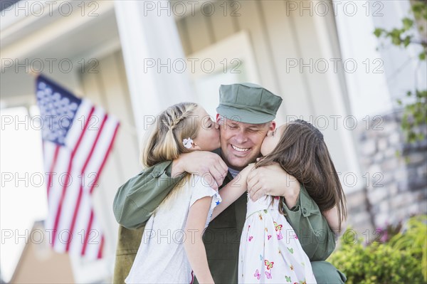 Returning Caucasian soldier hugging daughters