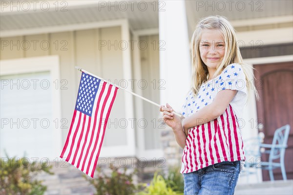 Smiling Caucasian girl waving American flag near house