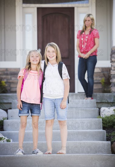 Caucasian sisters smiling on front steps on way to school