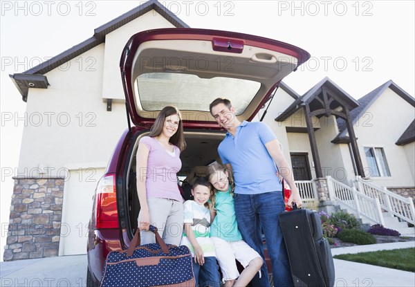 Caucasian family holding suitcases by car