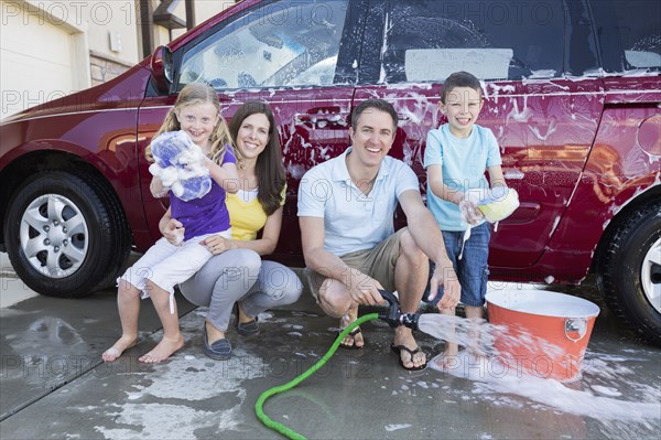 Caucasian family washing car in driveway