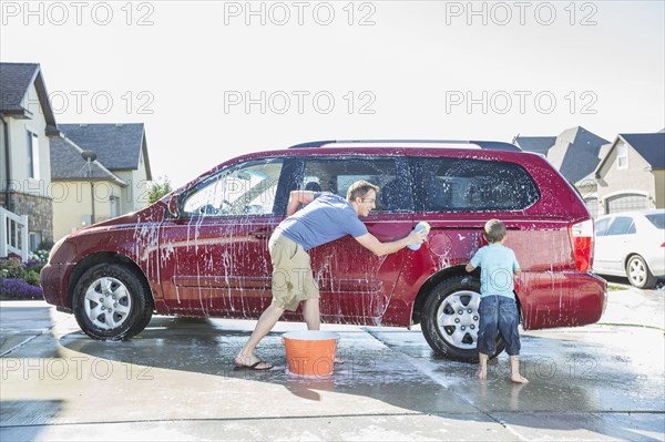 Caucasian father and son washing car in driveway