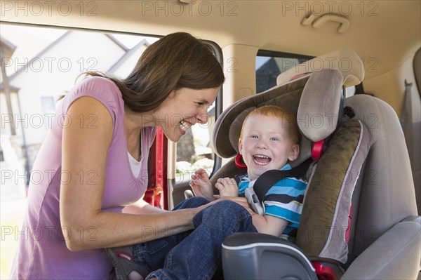 Caucasian mother fastening son into car seat