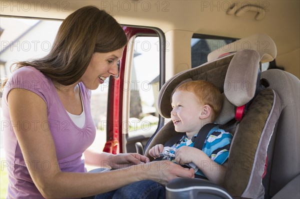 Caucasian mother fastening son into car seat