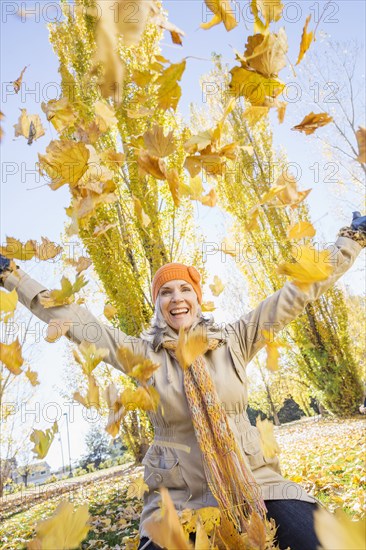 Older Caucasian woman playing in autumn leaves