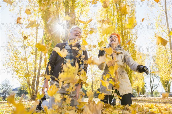 Older Caucasian couple playing in autumn leaves