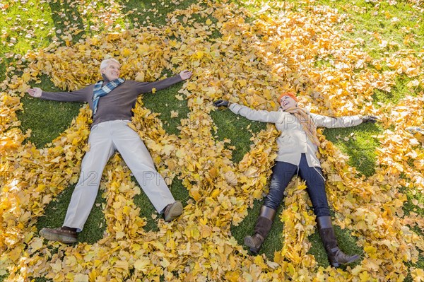 Older Caucasian couple playing in autumn leaves