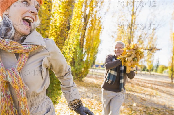 Older Caucasian couple playing with autumn leaves
