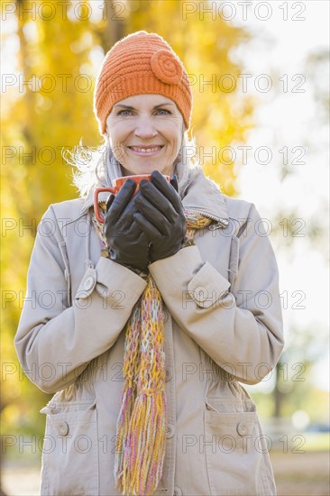 Older Caucasian woman drinking coffee near autumn trees