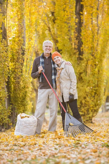 Older Caucasian couple raking autumn leaves