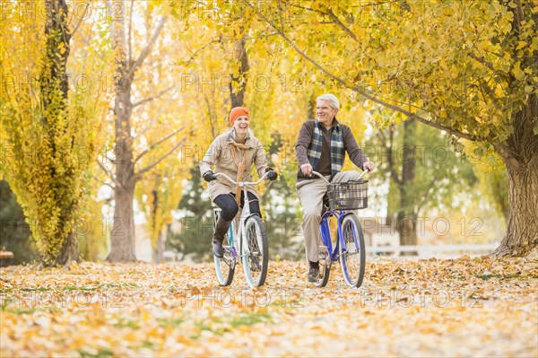 Older Caucasian couple riding bicycles on autumn leaves