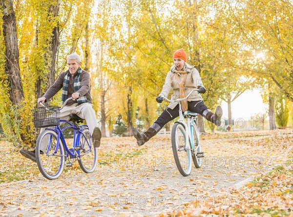 Older Caucasian couple riding bicycles on autumn leaves