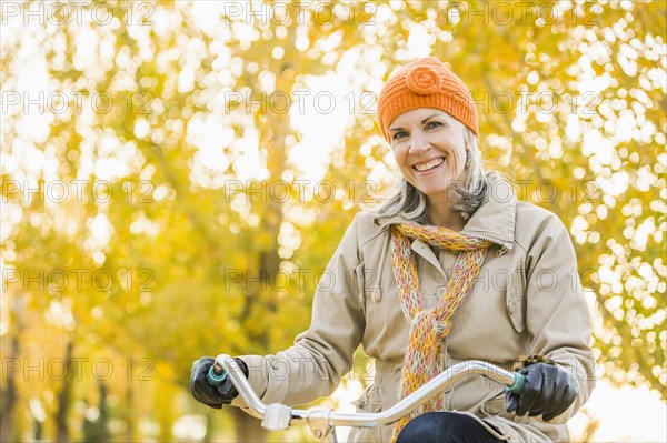 Older Caucasian woman riding bicycle under autumn trees