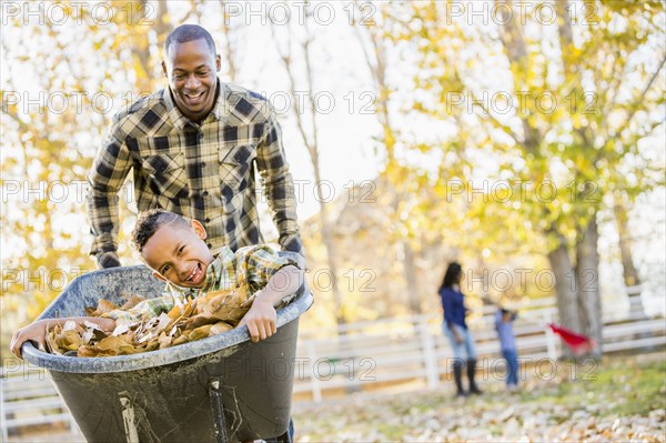 Father pushing son in wheelbarrow in autumn leaves