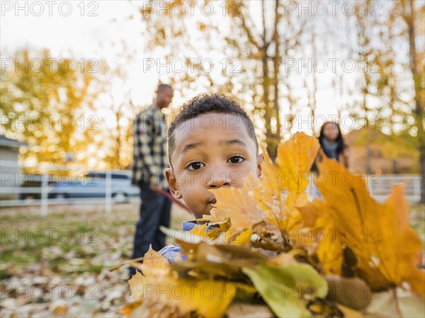 Black boy holding bundle of autumn leaves