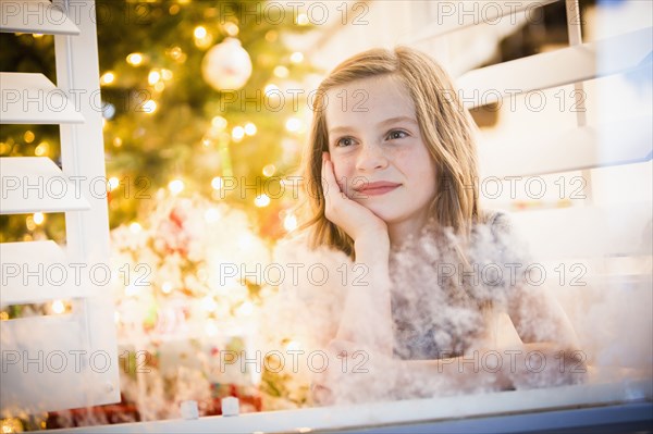 Caucasian girl peering out window at Christmas