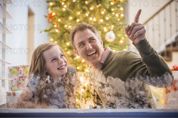 Caucasian father and daughter peering out frosty window at Christmas