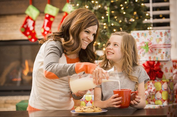 Caucasian mother and daughter leaving cookies and milk for Santa at Christmas