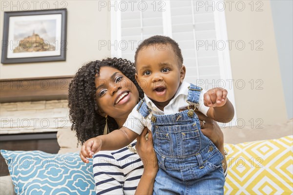 Black mother holding baby son on sofa