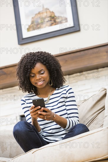 Black woman using cell phone on sofa