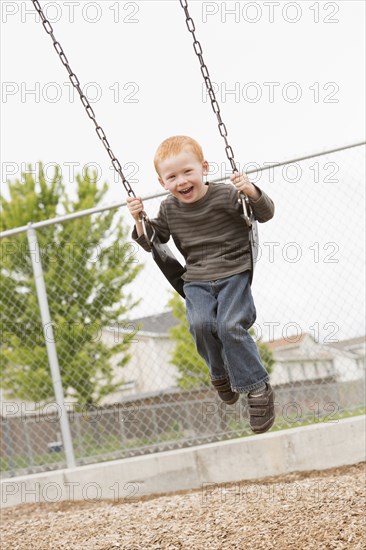 Caucasian boy sitting on playground swing