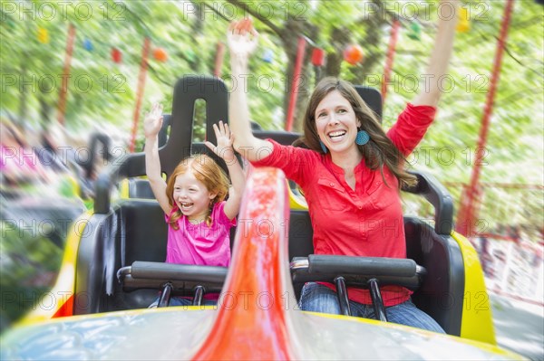 Mother and daughter riding roller coaster in amusement park