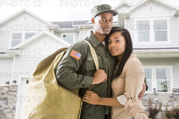 Returning soldier and wife standing outside house
