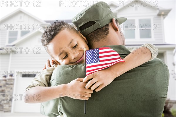 Soldier hugging patriotic son outside house