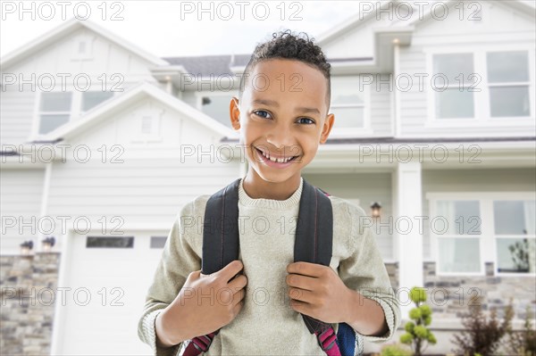 Black boy in backpack smiling outside house